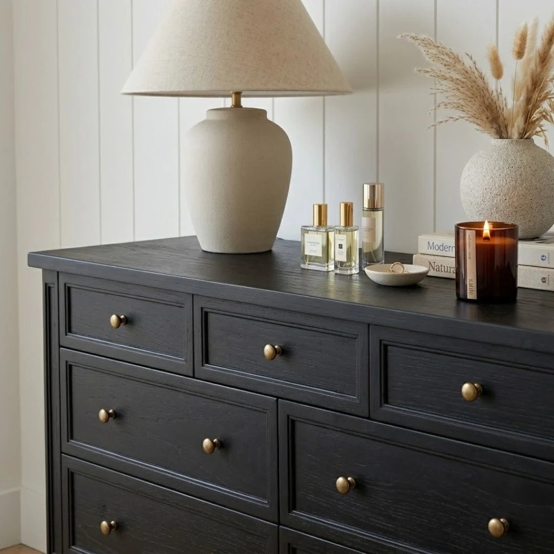 Dark wooden dresser with decorative items including a lamp, candles, and bottles on top.