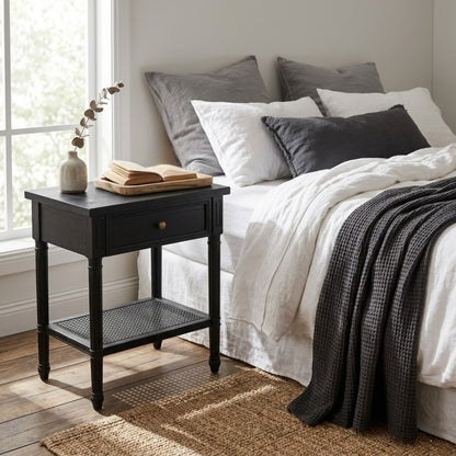 Bedroom with a bed featuring pillows and a blanket, next to a black nightstand with a book and vase.