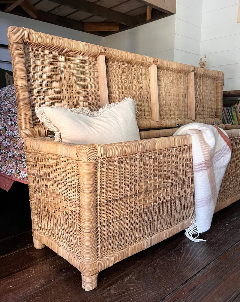 Wicker bench with cushions and a blanket on a wooden floor