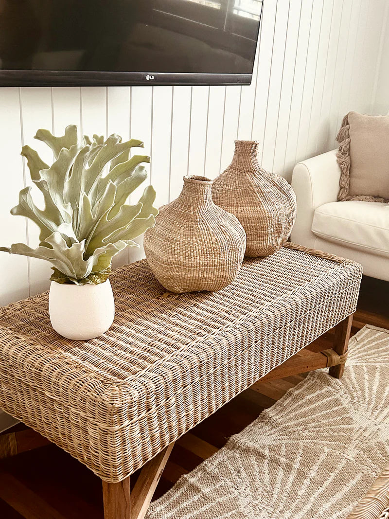 Wicker bench with decorative vases and a plant in a living room setting.