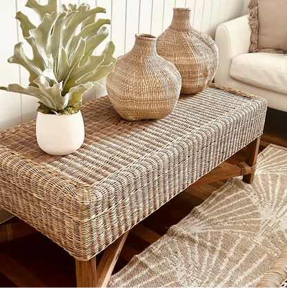 Wicker bench with decorative vases and a plant in a living room setting.
