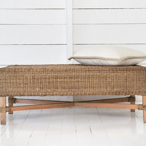 Wicker bench with a cushion against a white wooden panel background