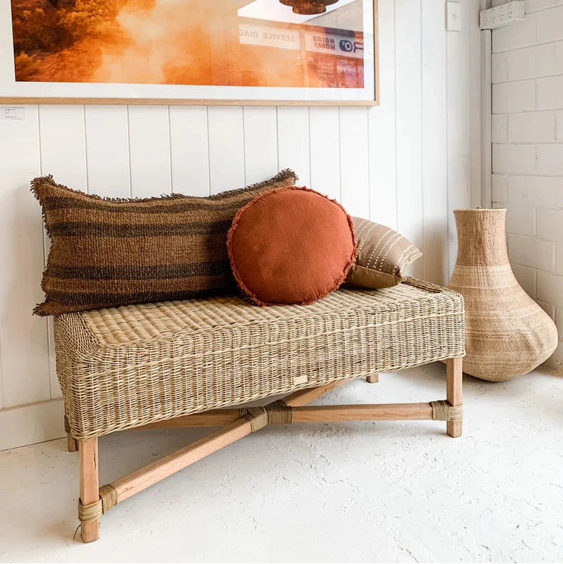 Wicker bench with decorative pillows in a room with a large framed picture on the wall.
