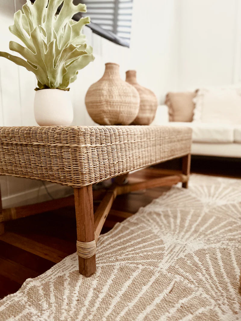 Wicker coffee table with decorative vases and a plant in a living room setting.