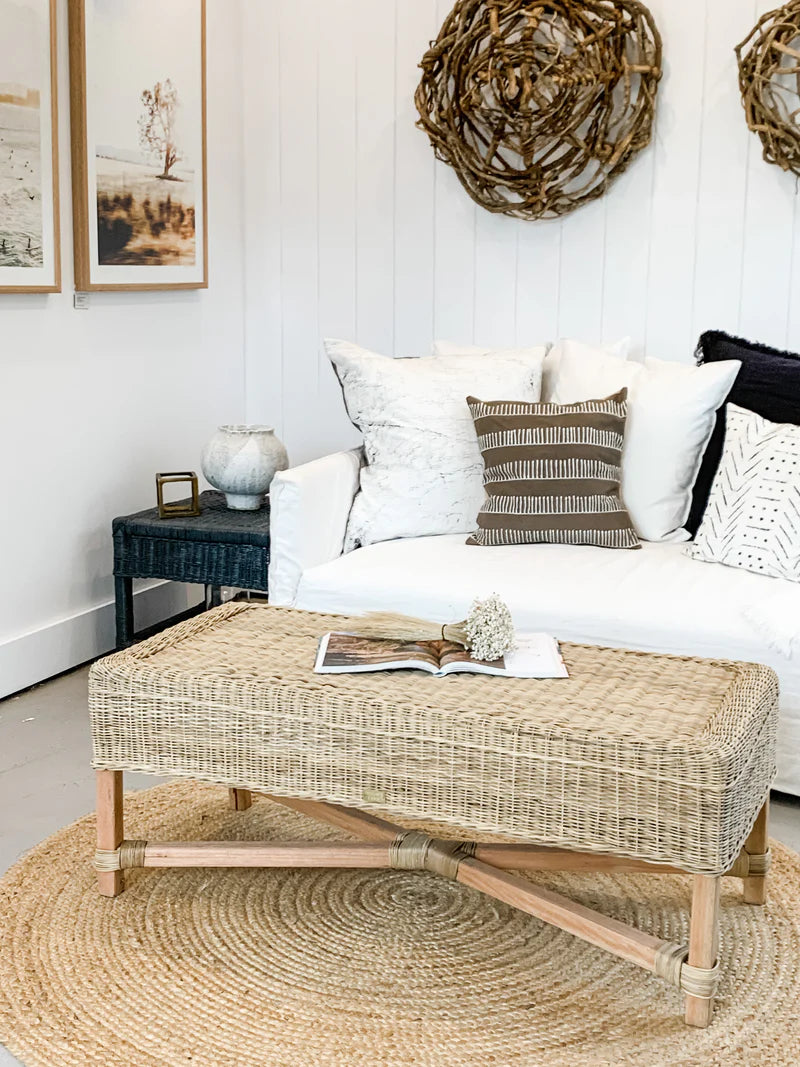 Living room with a white sofa, wicker ottoman, and decorative elements.