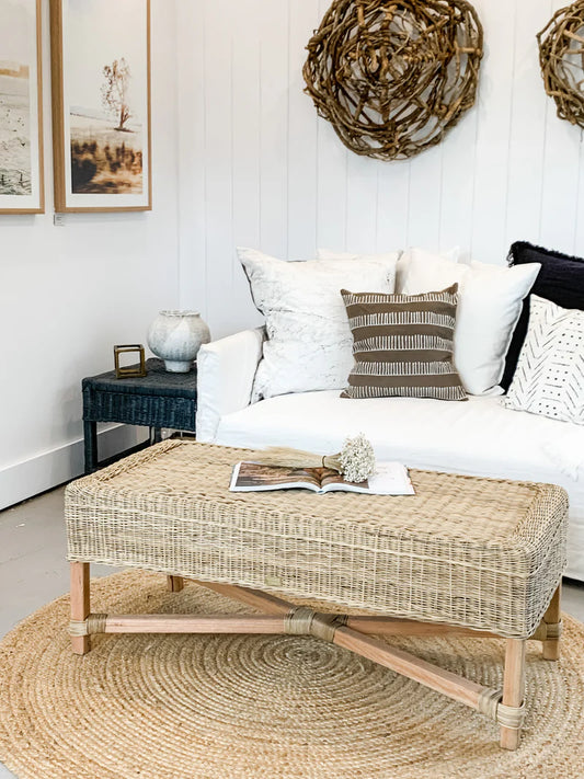 Living room with a white sofa, wicker ottoman, and decorative elements.