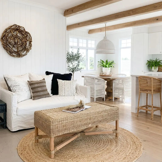 Cozy living room with white sofa, wicker ottoman, and wooden beams.
