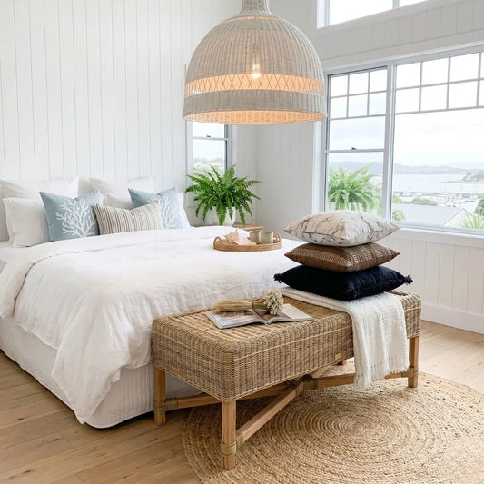 Cozy bedroom with a bed, wicker bench, and large windows.