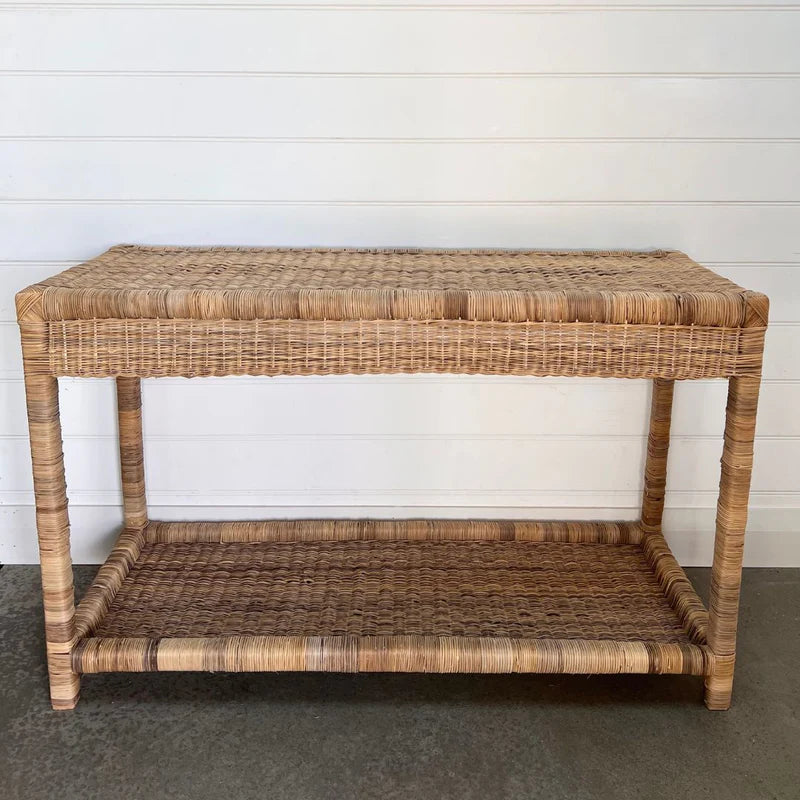 Wicker side table with a shelf against a white wall.