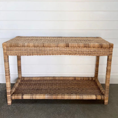 Wicker side table with a shelf against a white wall.