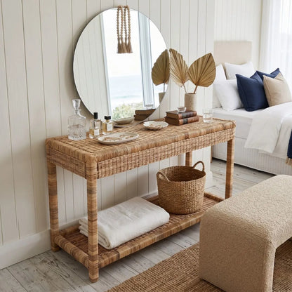 Wicker console table in a bedroom room with decor items and a round mirror.