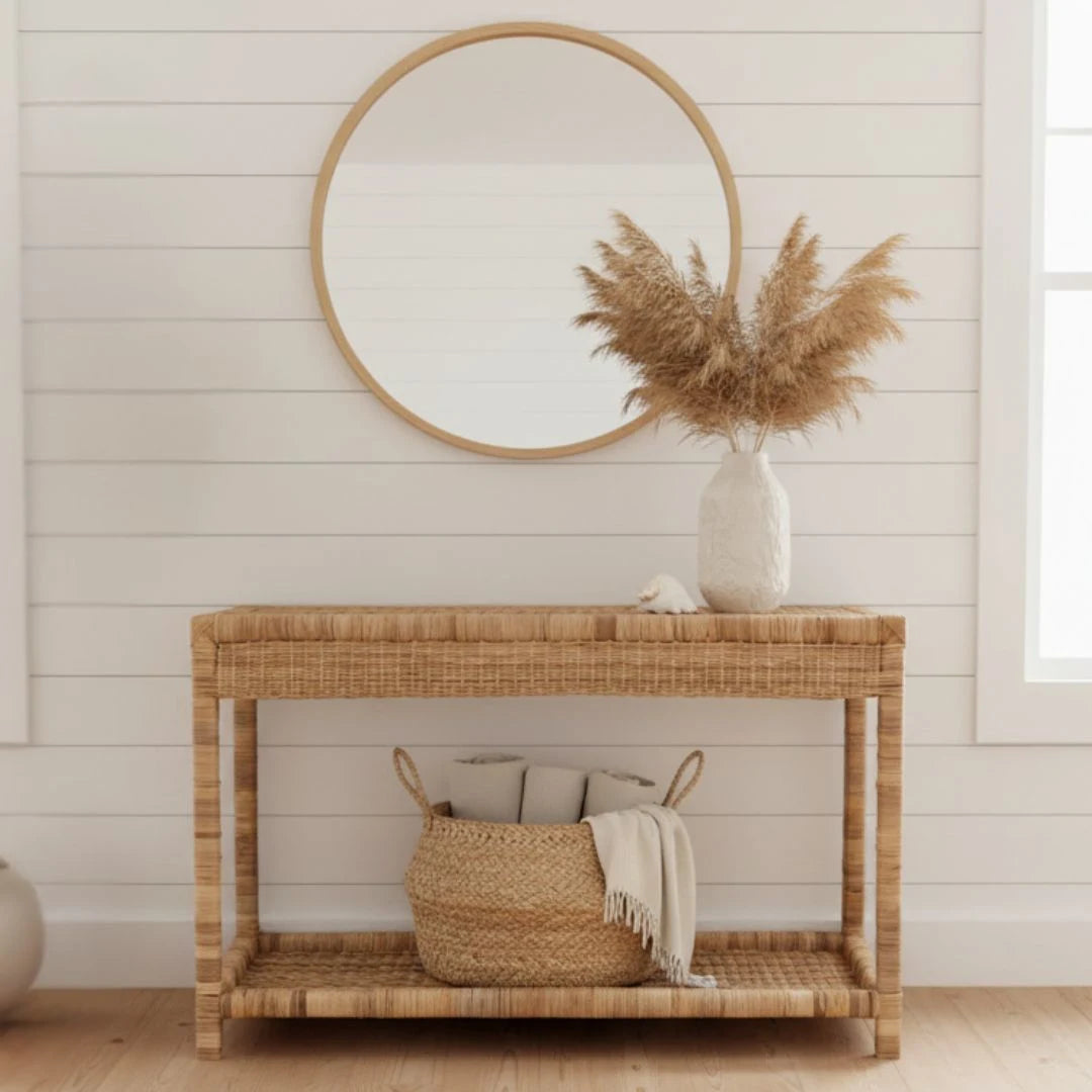 Rattan console table with a round mirror and decorative items in a room with wooden flooring.