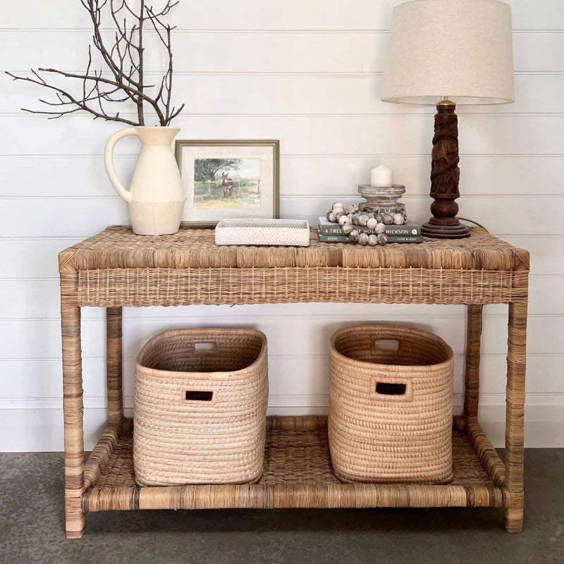 Wicker console table with decorative items against a white wall.