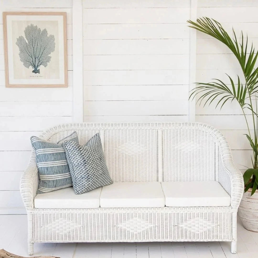 White wicker sofa with striped cushions against a white wall with a plant and artwork.