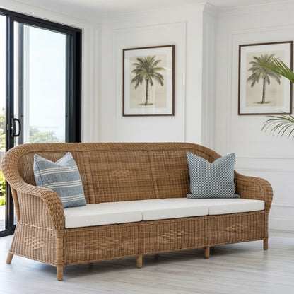Wicker sofa with white cushions in a room with large windows and plants