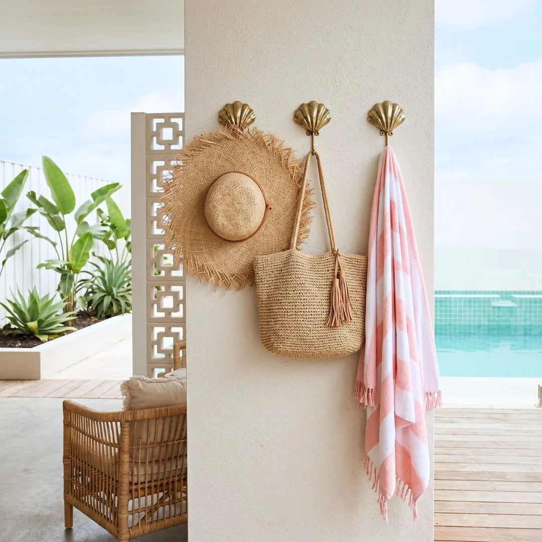 Decorative wall with shell hooks holding a straw hat, bag, and pink towel by a poolside.