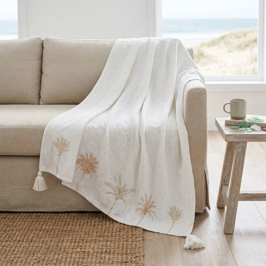 Beige sofa with a white blanket featuring floral patterns in a bright room.