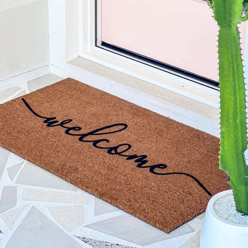 Doormat with 'welcome' text in a home entranceway with a cactus plant.