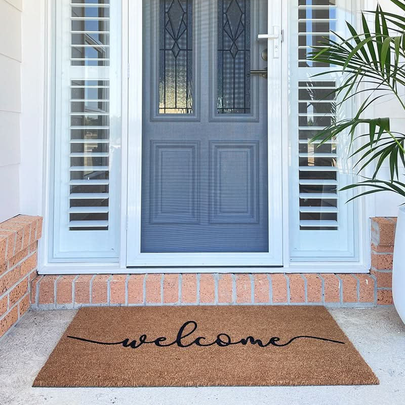 Front door with a 'welcome' mat and plant on a porch