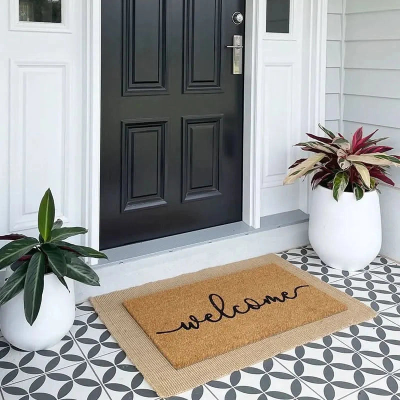 Front door with a 'welcome' mat, plants, and decorative tiles.