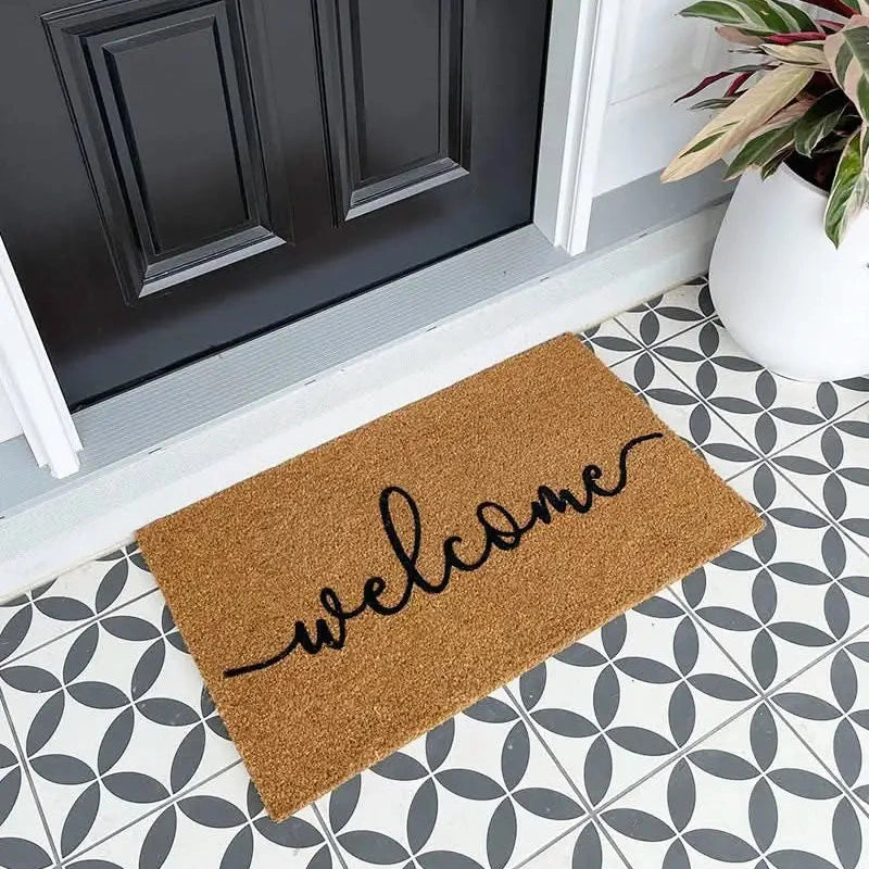 Doormat with 'welcome' text on a patterned floor in front of a black door.