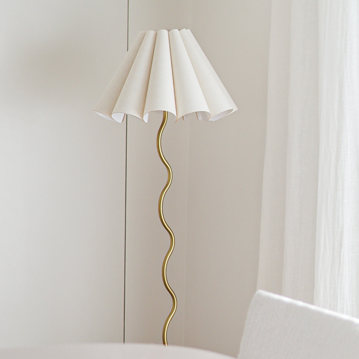 Modern floor lamp with white shade and gold curved base against a neutral wall.
