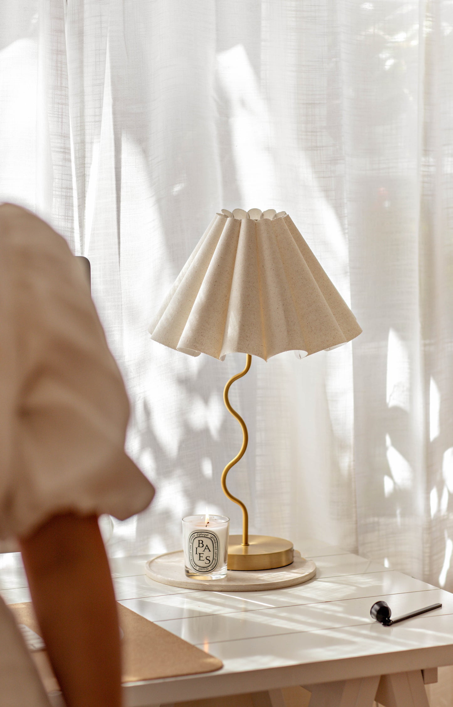 Beige lamp on a table with a candle and notebook, draped curtains in the background