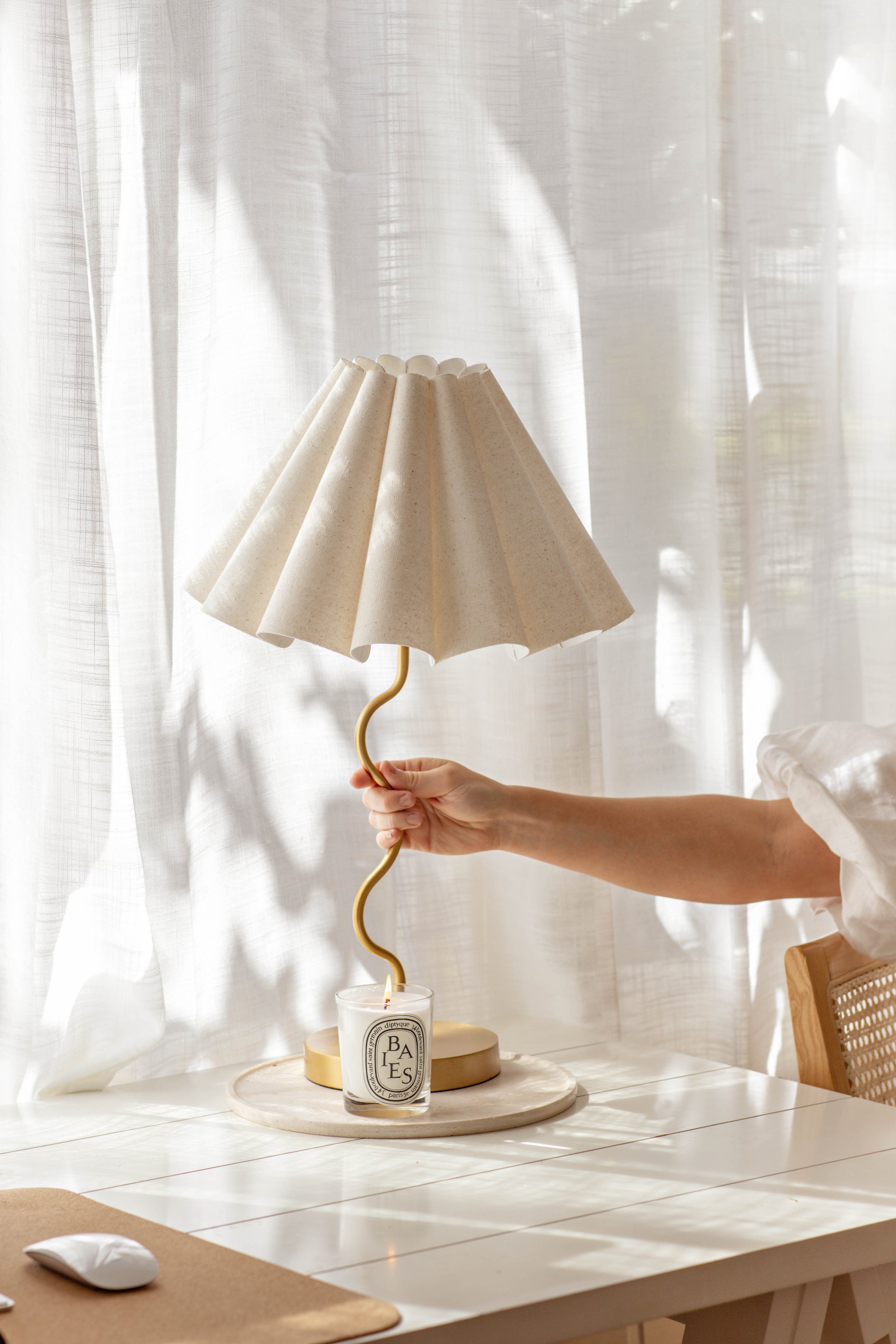 Person holding the cora table lamp with a white shade on a light-colored surface with a white curtain background