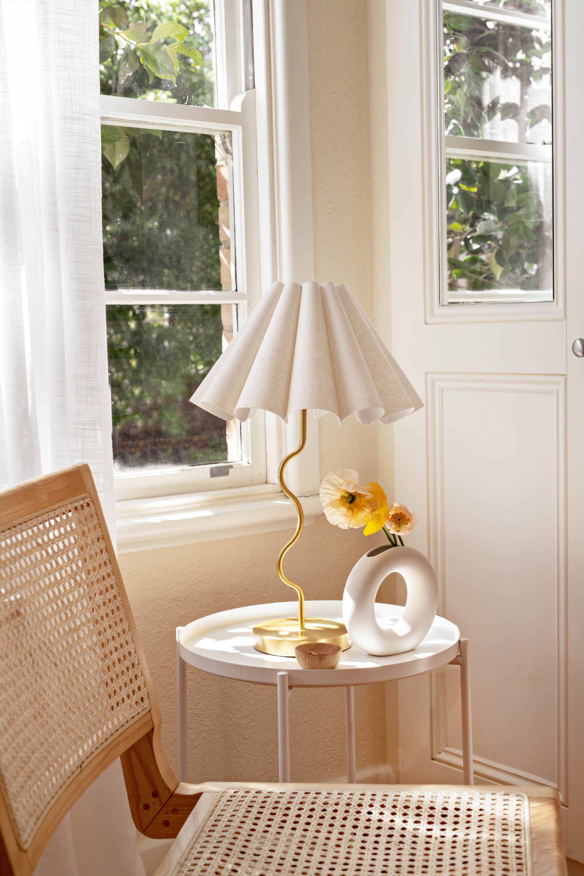 Small round table with a lamp and vase by a window in a bright room