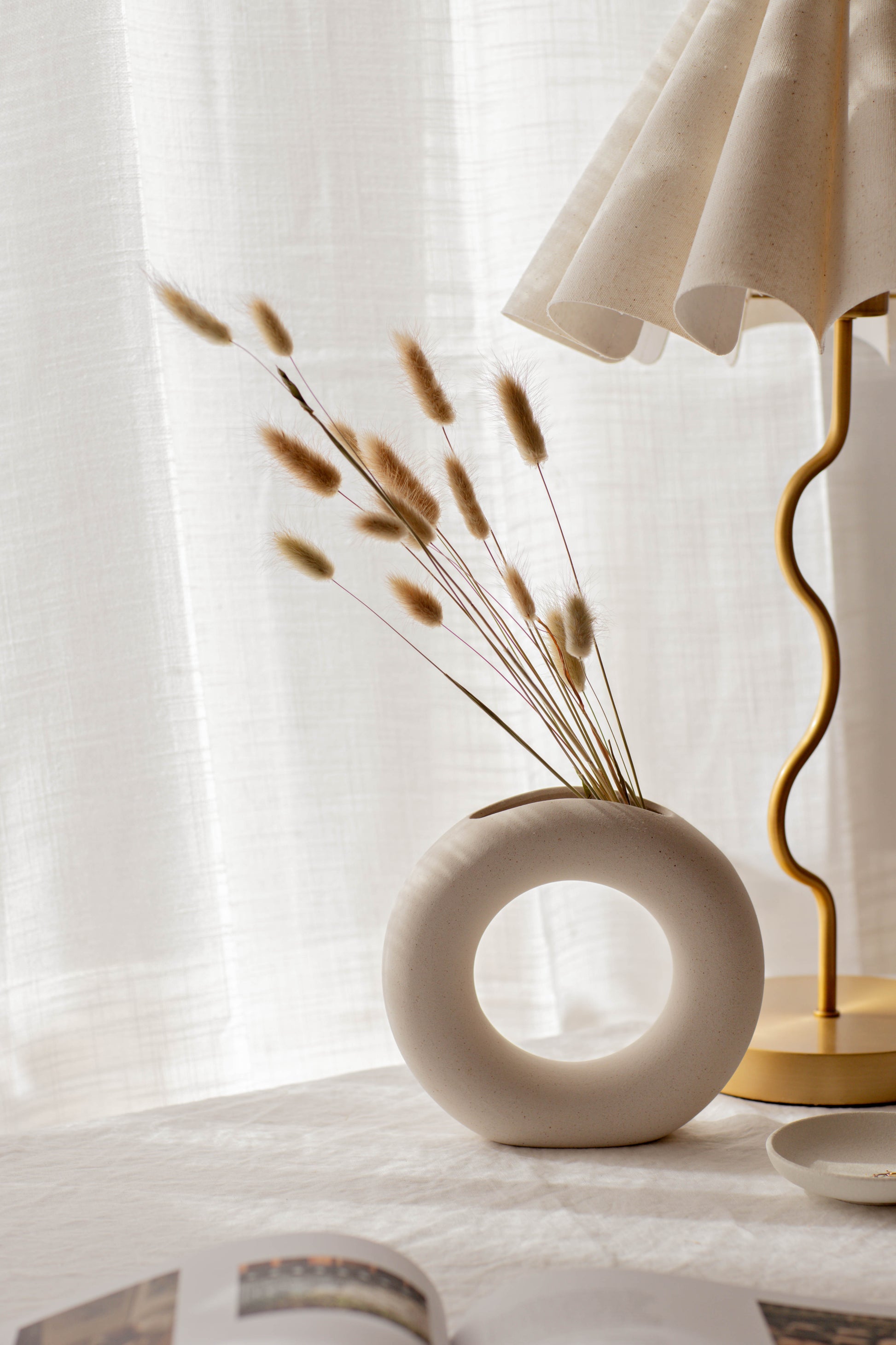 White vase with dried plants on a table next to a lamp with a white shade.