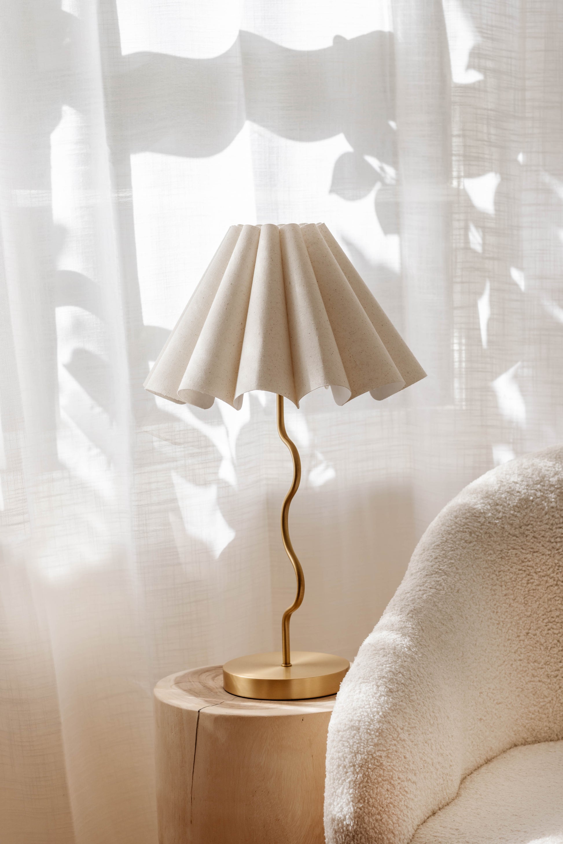 Cora lamp on a wooden side table with a soft white curtain in the background