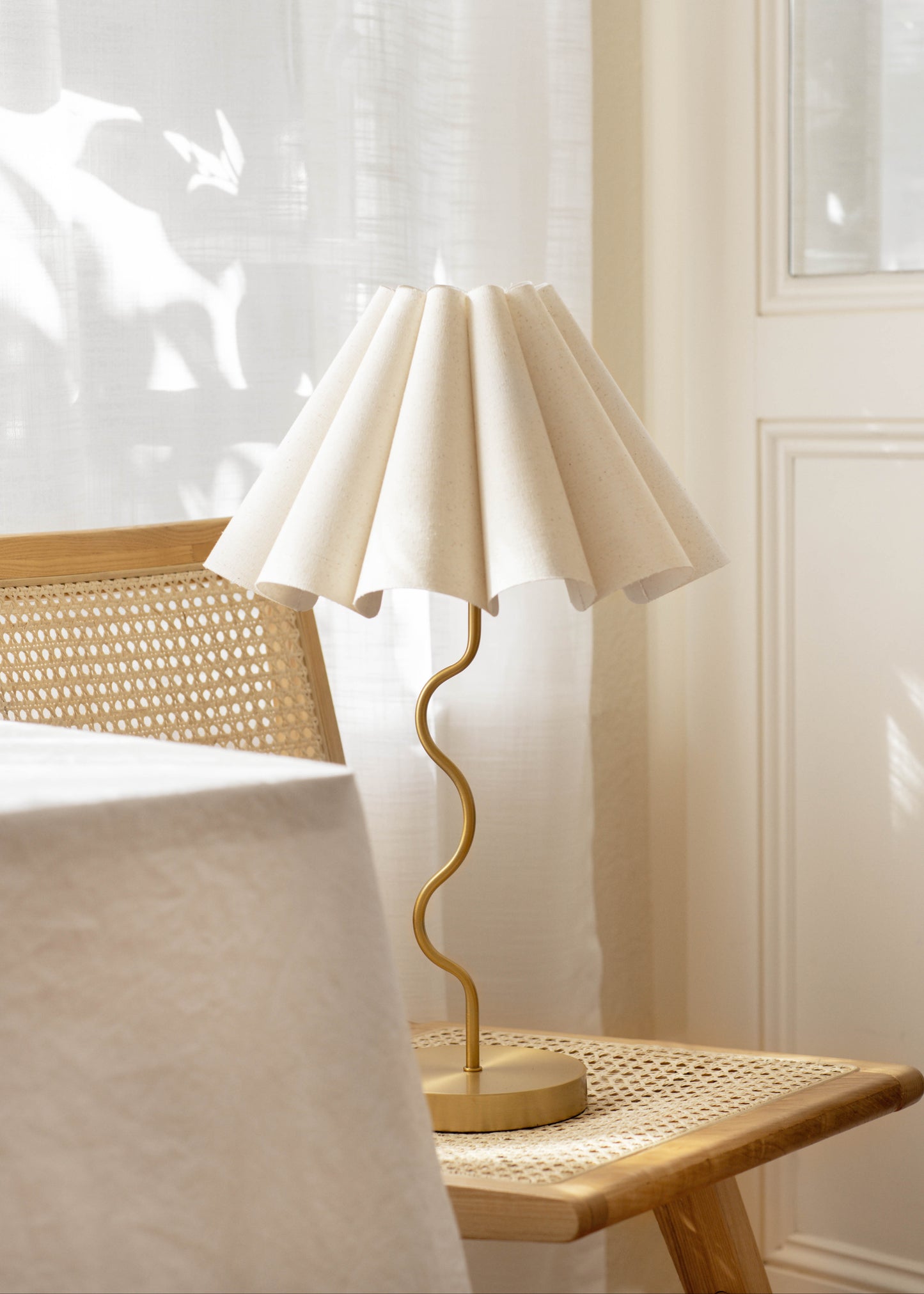 Table lamp with a white shade on a wooden table in a softly lit room.