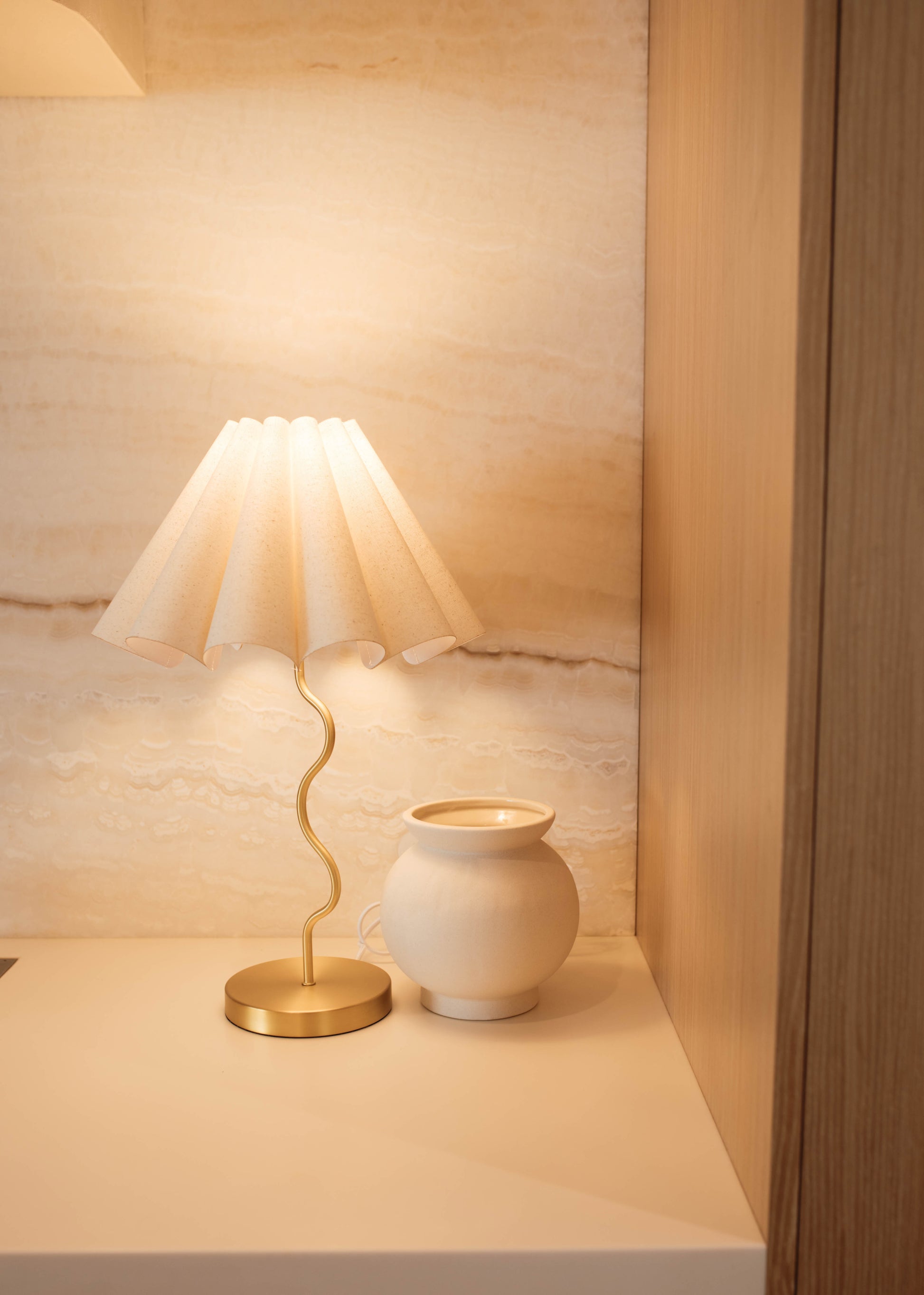Small lamp and white vase on a wooden shelf with a light wood panel background