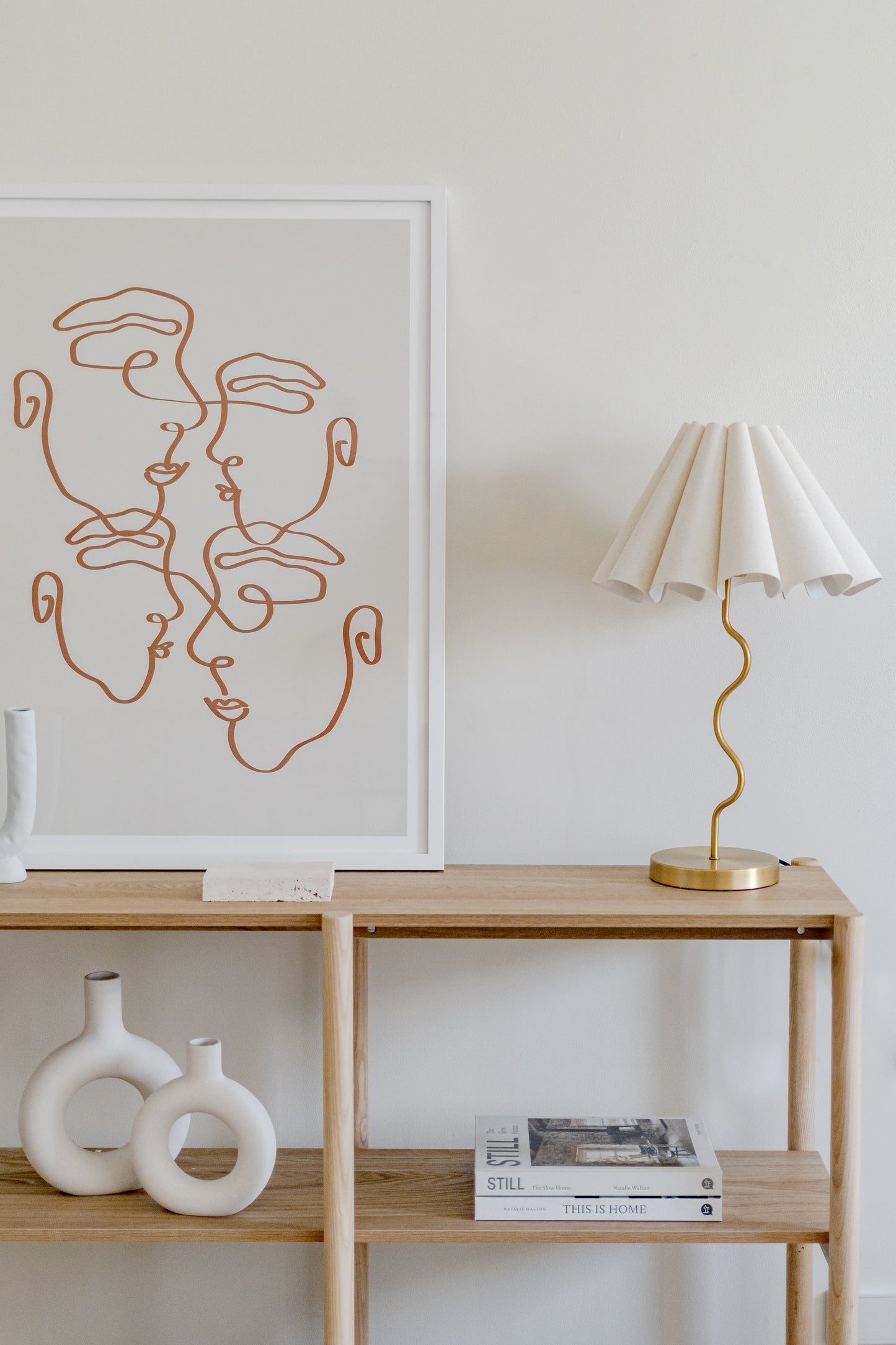 Modern interior with a wooden shelf, lamp, and abstract art on a white wall.