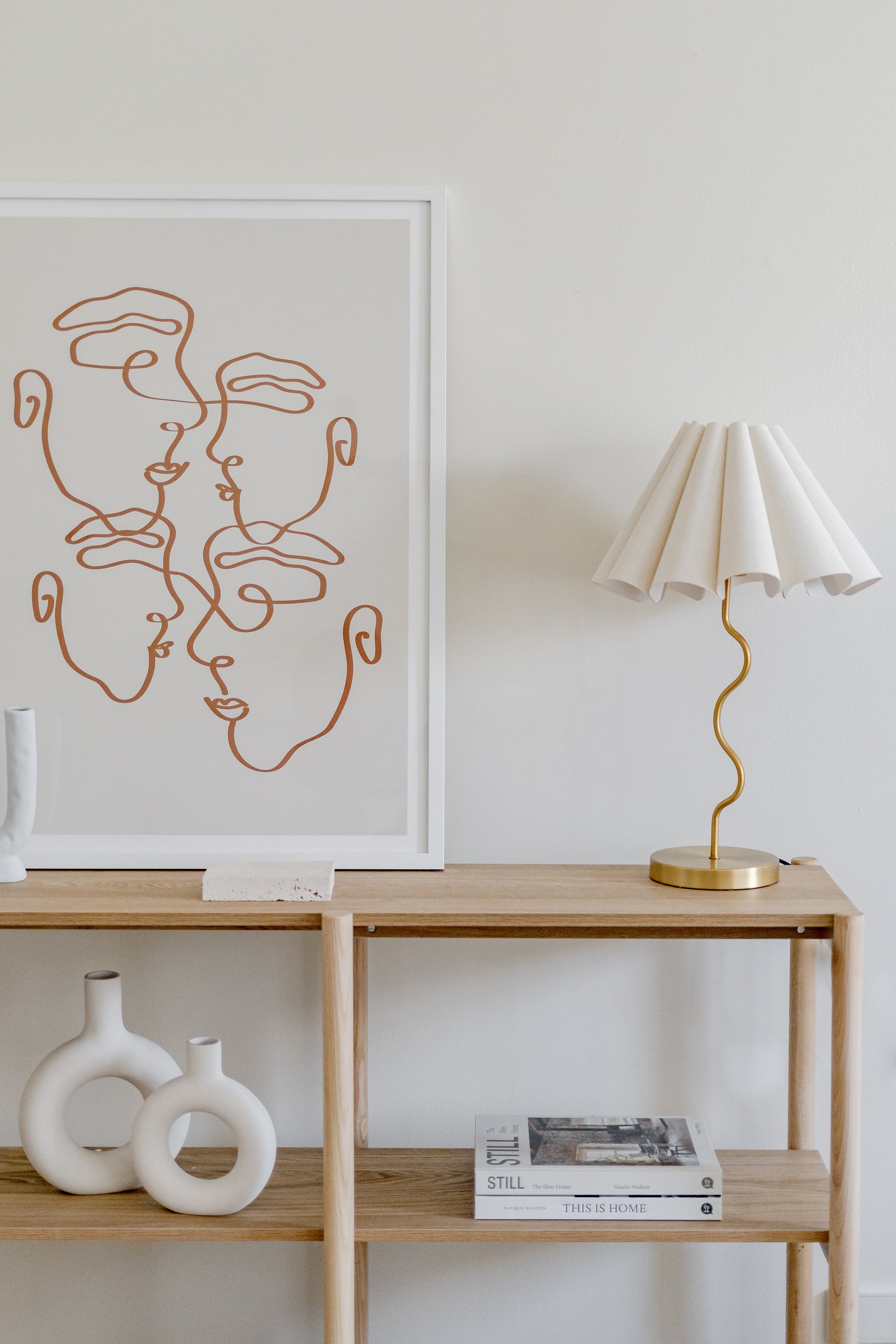 Modern interior with a wooden shelf, lamp, and abstract art on a white wall.