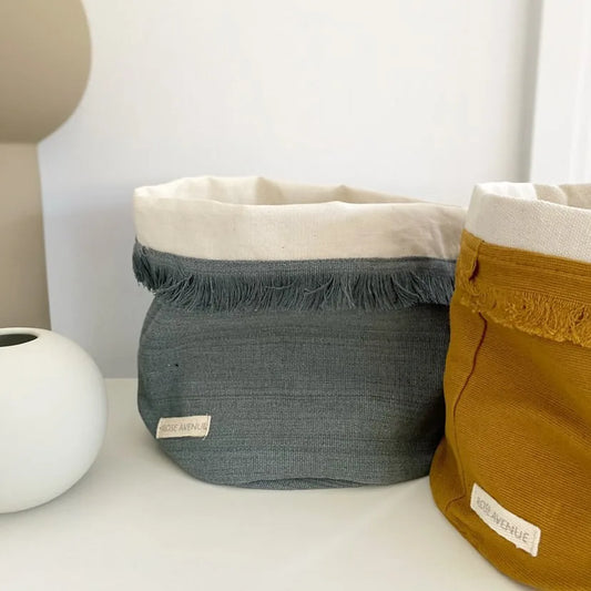 Two fabric baskets, one gray and one mustard yellow, on a white surface with a neutral background.