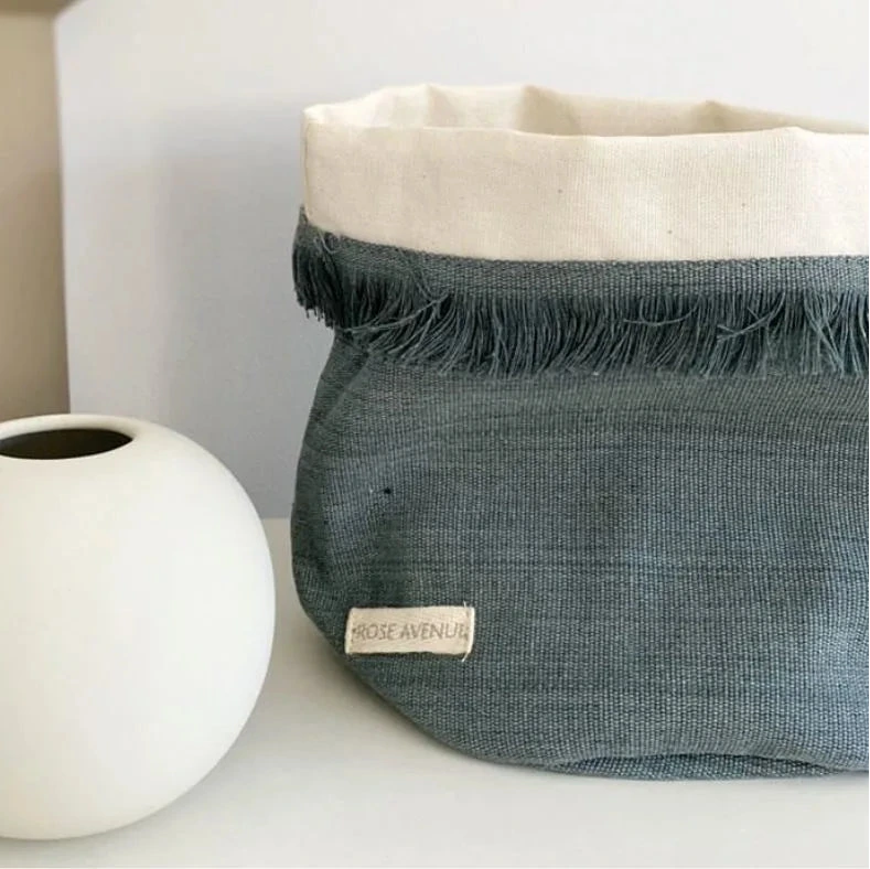 Textile basket with frayed edge and white interior next to a white spherical vase on a light surface.
