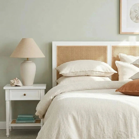 Bedroom with a bed featuring white bedding and brown pillows, a nightstand with a lamp, and a woven basket.