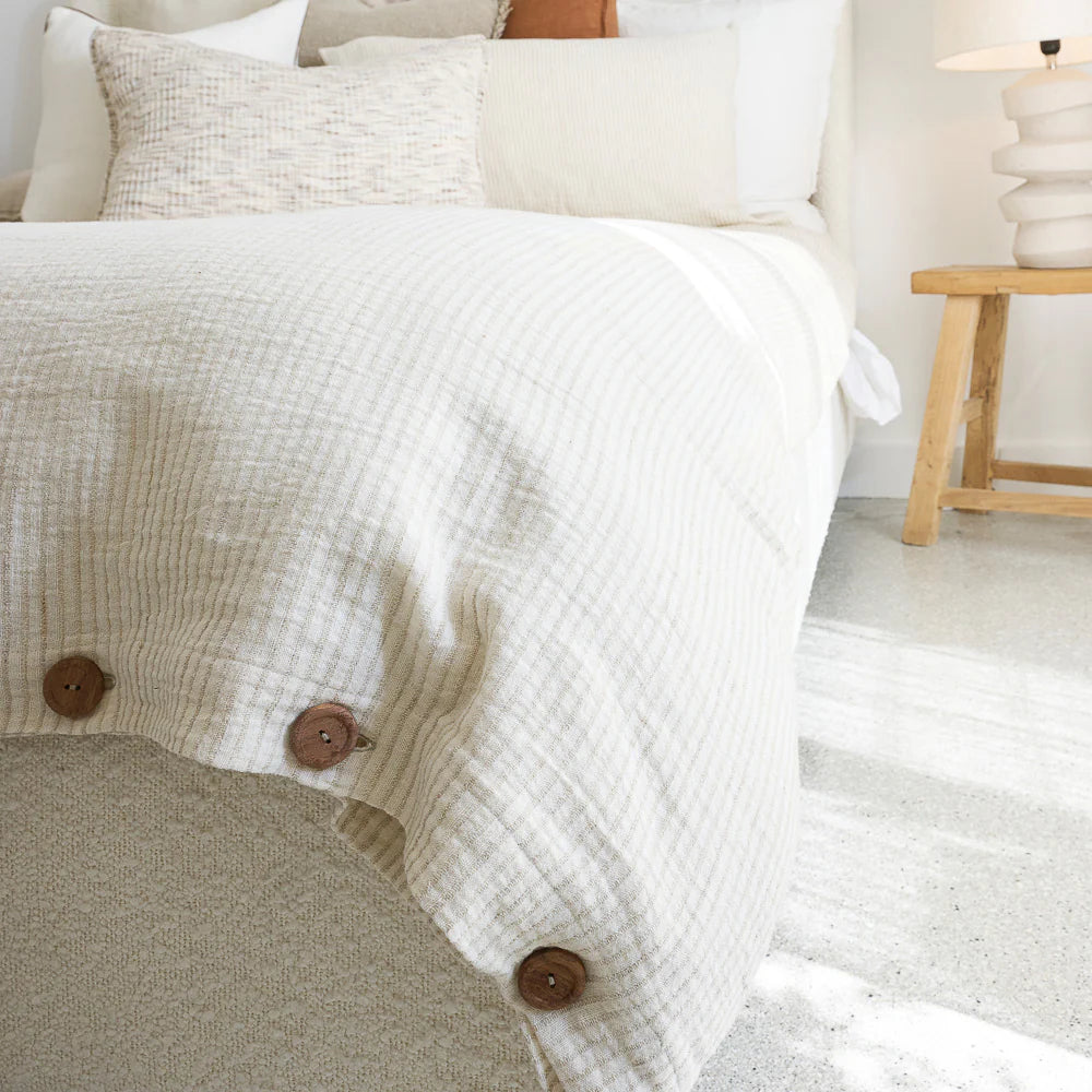 Cotton duvet cover in off white and natural pin stripe with button details on a bed in a bedroom setting.