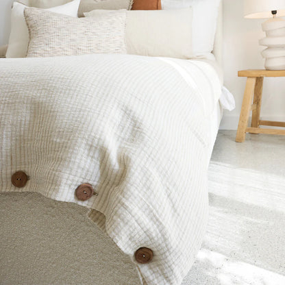 Cotton duvet cover in off white and natural pin stripe with button details on a bed in a bedroom setting.