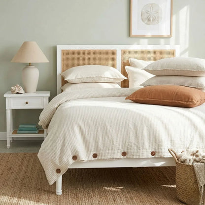 Bedroom with a bed featuring white bedding and brown pillows, a nightstand with a lamp, and a woven basket.