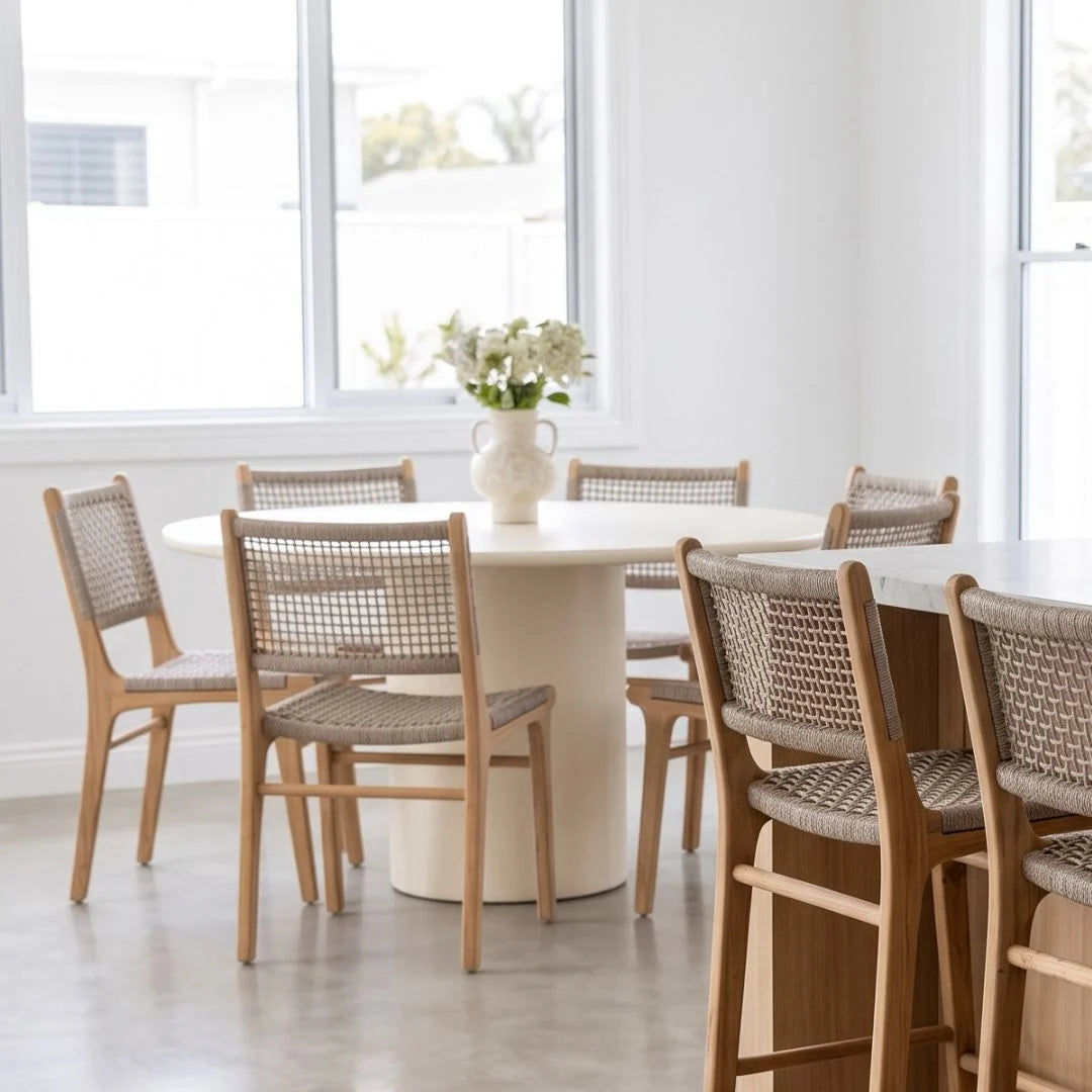 Round white dining table with wooden chairs in a bright room with large windows.
