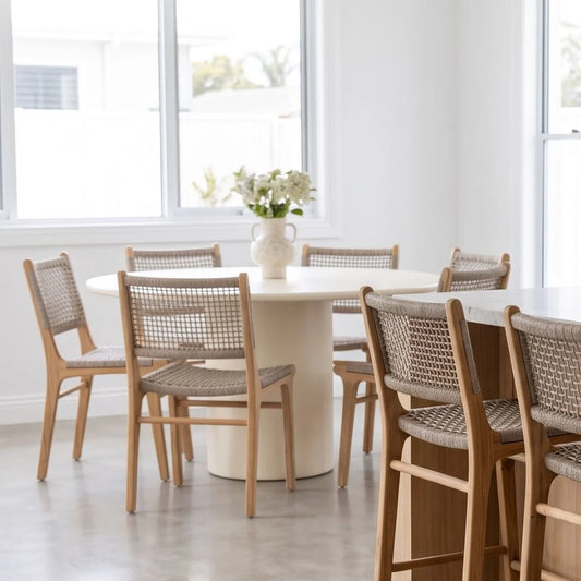 Round white dining table with wooden chairs in a bright room with large windows.