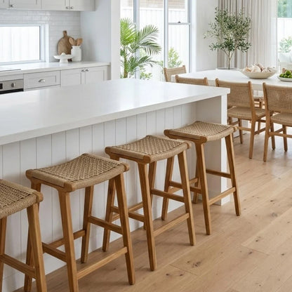 Wooden bar stools in a modern kitchen with white countertops and large windows.
