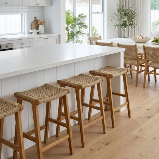 Wooden bar stools in a modern kitchen with white countertops and large windows.