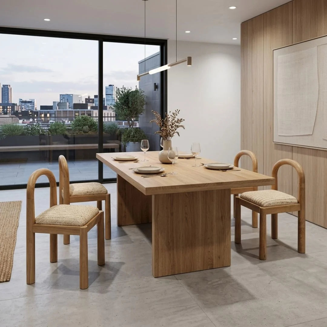 Dining area with wooden table and chairs in a modern room with large windows.