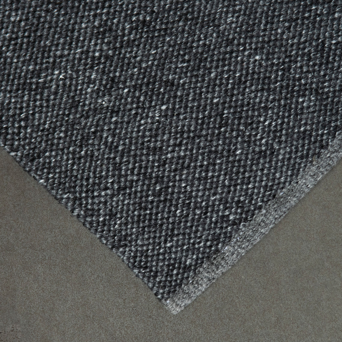 Close-up of a textured eco grey rug corner on a neutral background