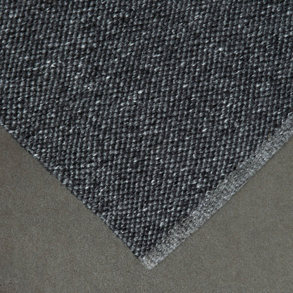 Close-up of a textured eco grey rug corner on a neutral background