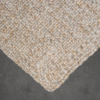 Close-up of a textured beige rug corner on a dark surface