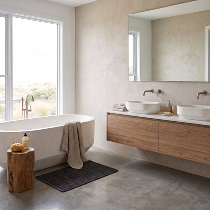 A modern bathroom interior with a freestanding oval bathtub, double vessel sinks on a floating wood vanity, large mirror, concrete floor, and a window overlooking an outdoor landscape.